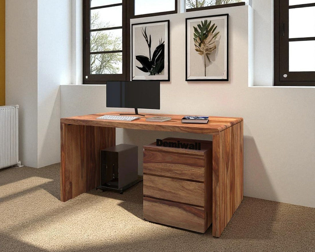Wooden desk with computer setup in a bright room with large windows.