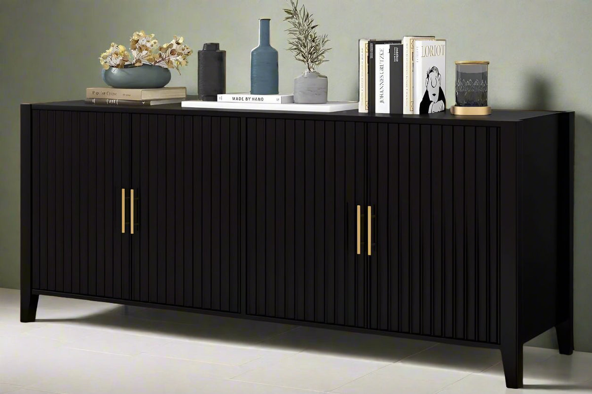 Black solid wood storage cabinet with metal handles, four doors, and gold-colored accents, placed against a backdrop featuring books, a vase, and other decor items.