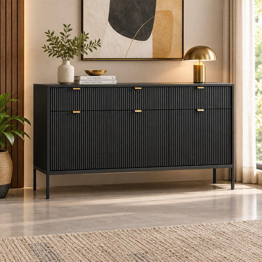 A modern black ribbed console cabinet with gold drawer pulls, styled in a warm beige living room with a gold table lamp, books, and a vase on top.