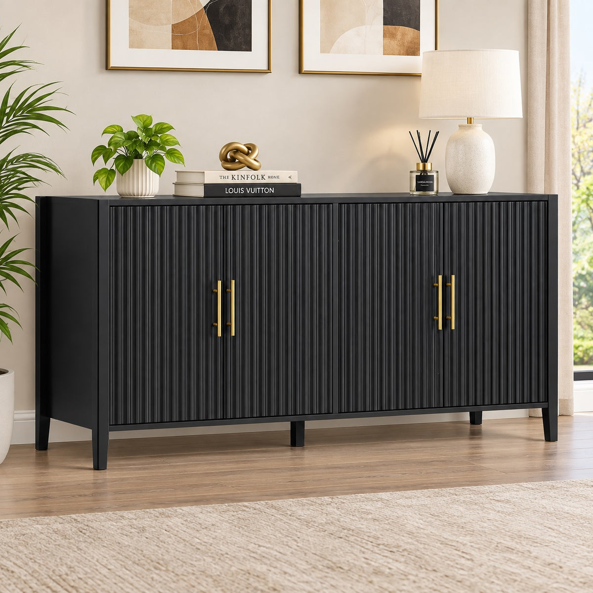 A modern black sideboard cabinet with vertical fluting and gold handles, styled in a bright living room setting with a lamp, plant, and decorative items on top.