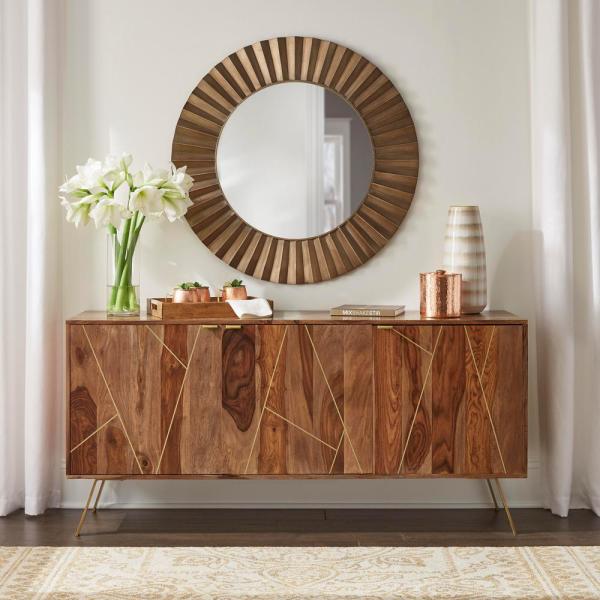 A mid-century modern wooden sideboard cabinet with geometric gold inlay on the doors, styled in a warm, decorated room with plants, books, and a small bicycle decor piece.